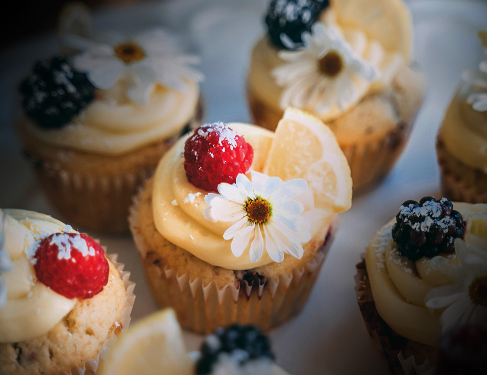 Cupcakes with creamy custard frosting adorned with berries, orange and flowers
