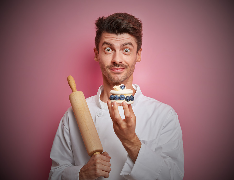A man in a chefs uniform holding a cake